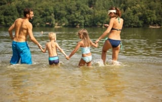 family in swimsuits walking into a lake