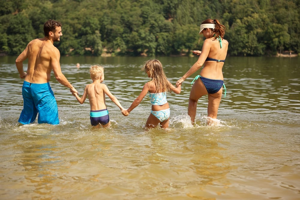 family in swimsuits walking into a lake