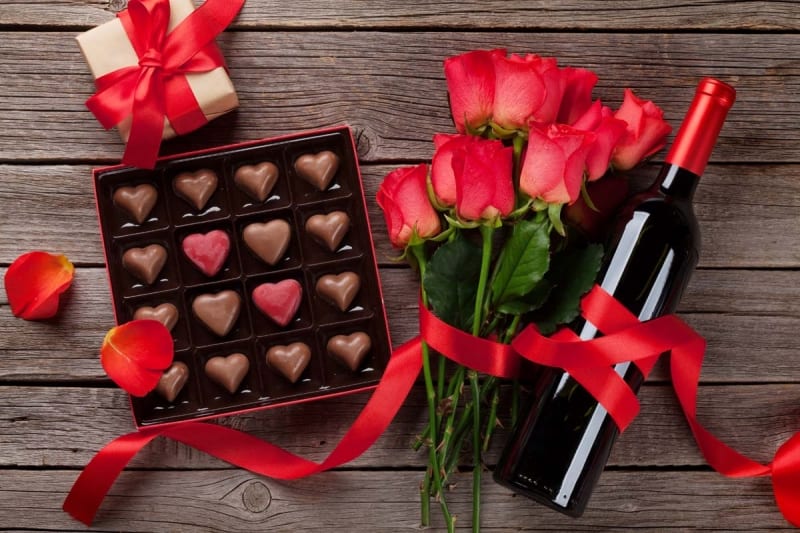 Valentines day with red roses, wine bottle and chocolate box on wooden table.